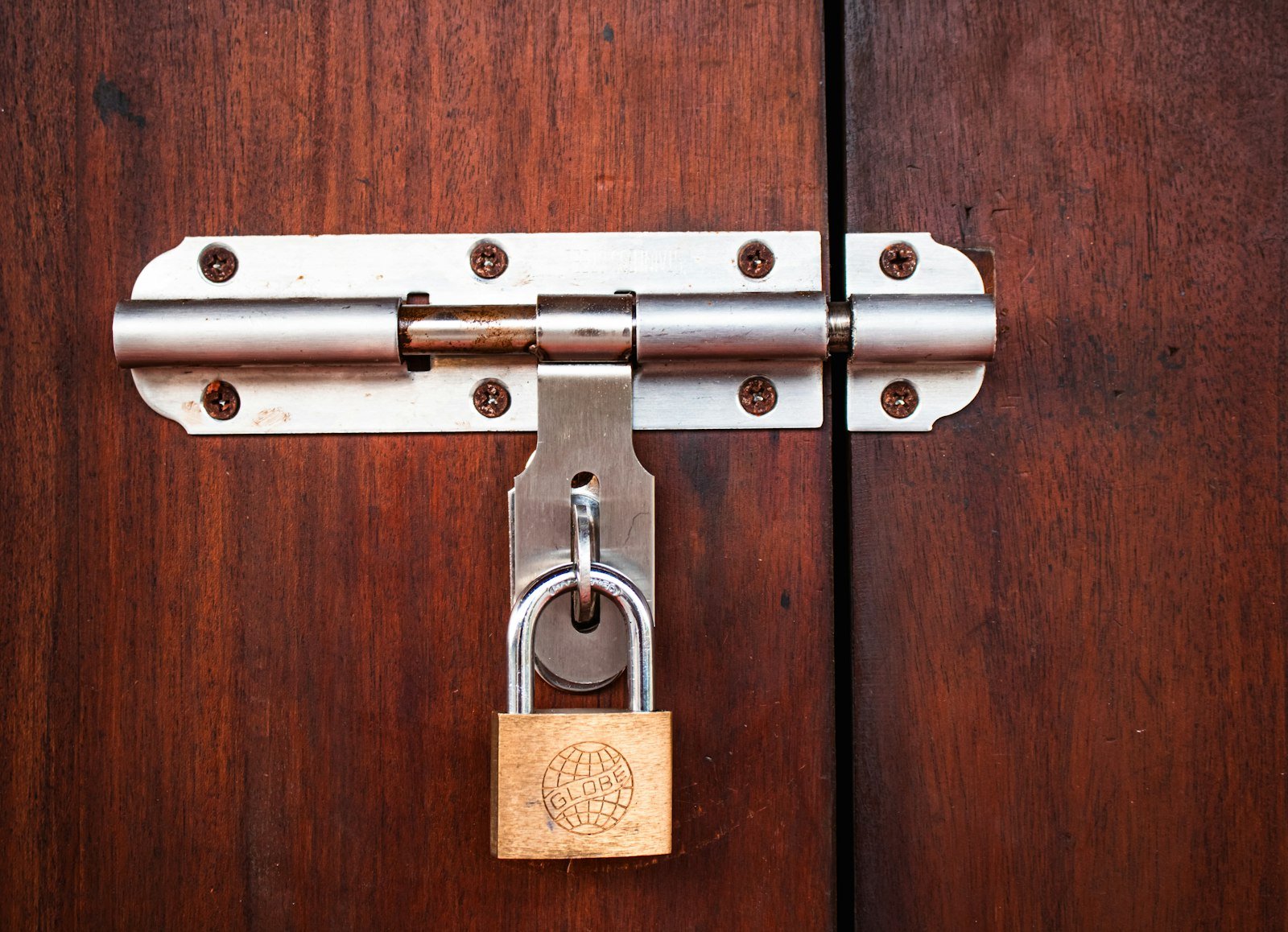 Brass Globe padlock securing a sliding bolt on a timber door
